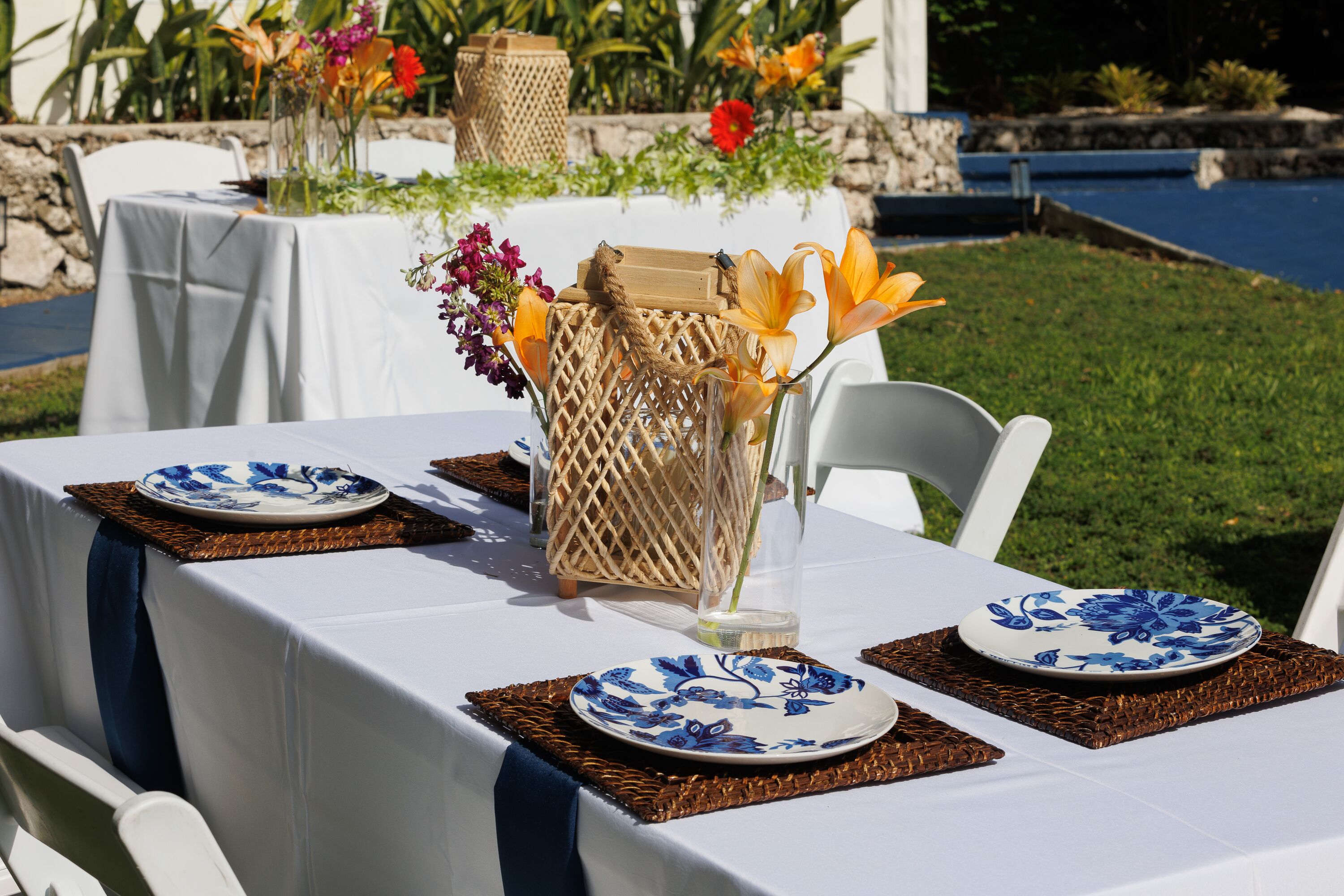 Montaje de comedor al aire libre con manteles blancos, platos florales azules y caminos de mesa tejidos.
