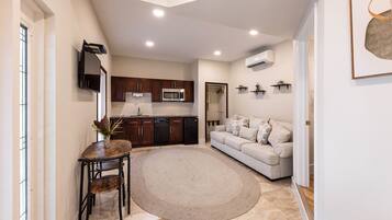 A compact living space with a kitchenette, a sofa, a dining table with chairs, and a decorative rug.