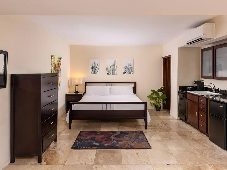 A bedroom with a bed, dresser, nightstand, lamp, and wall art.