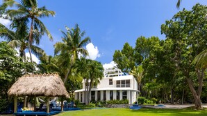 A white building with a pool, surrounded by palm trees and a thatched-roof structure. - Azul del Mar (Key Largo)