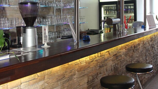 A bar area with a stone wall, a coffee machine, and a shelf with glasses and records.