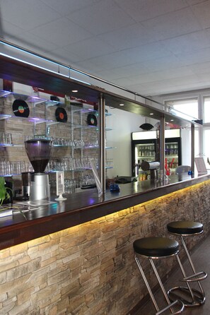 A bar area with a stone wall, a coffee machine, and a shelf with glasses and records. - Metropol Hostel Berlin (Berlin)