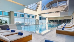 Ein moderner Poolbereich im Innenbereich mit Liegestühlen und freiem Blick auf die Stadtlandschaft.