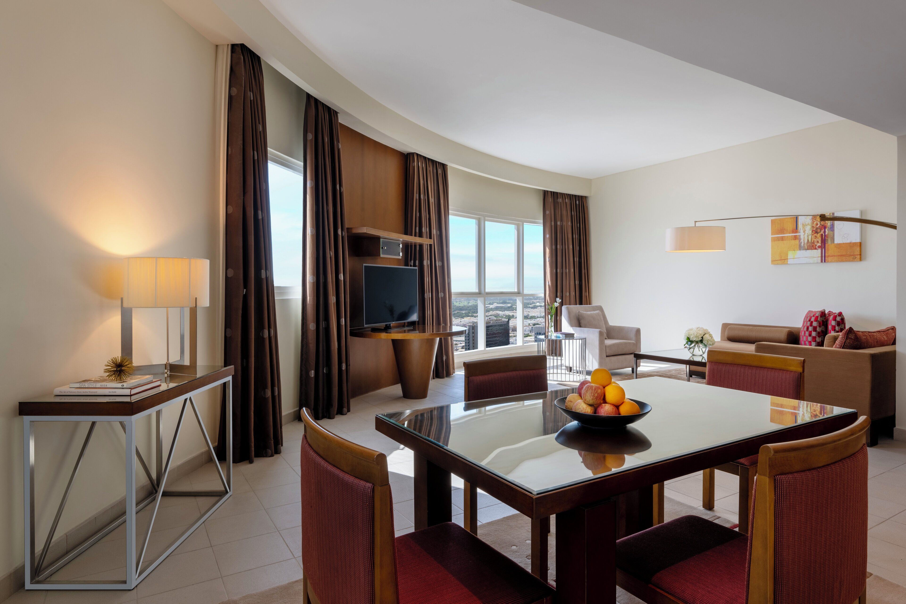 Quarto de hotel moderno com área de refeições, TV e sofá.