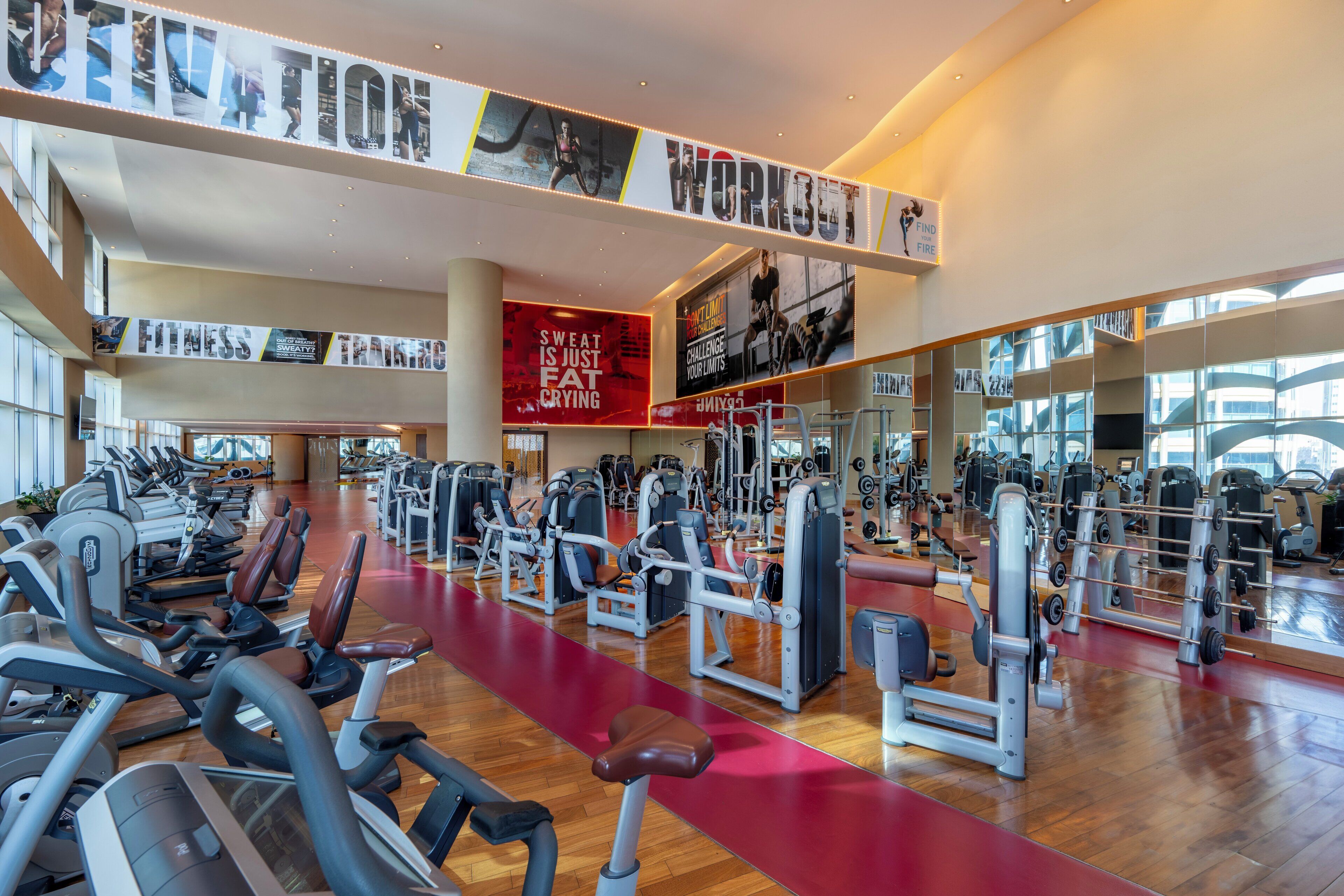 Une salle de sport spacieuse, équipée de divers appareils d’exercice, dotée d’une piste de course rouge et ornée d’affiches motivantes sur les murs.