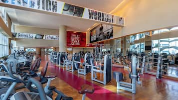 Une salle de sport spacieuse, équipée de divers appareils d’exercice, dotée d’une piste de course rouge et ornée d’affiches motivantes sur les murs.