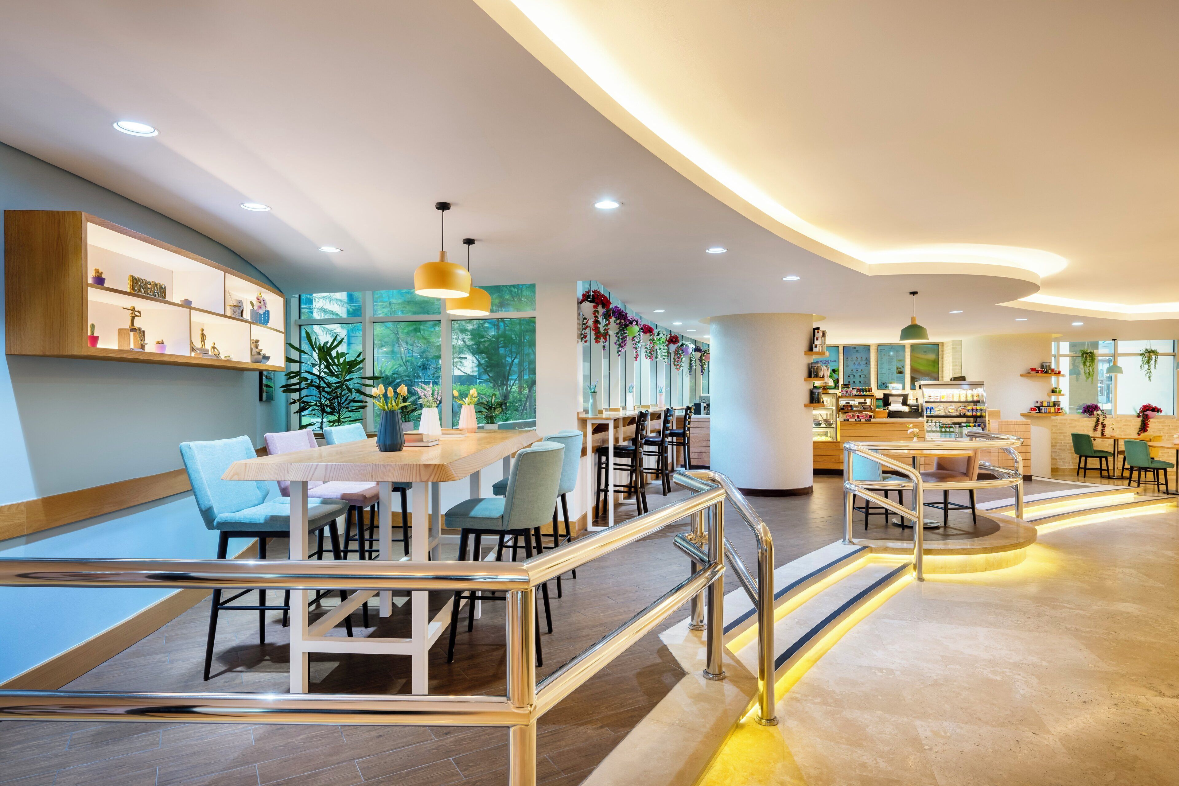 A modern hotel lobby with a central seating area, a bar, and a staircase.