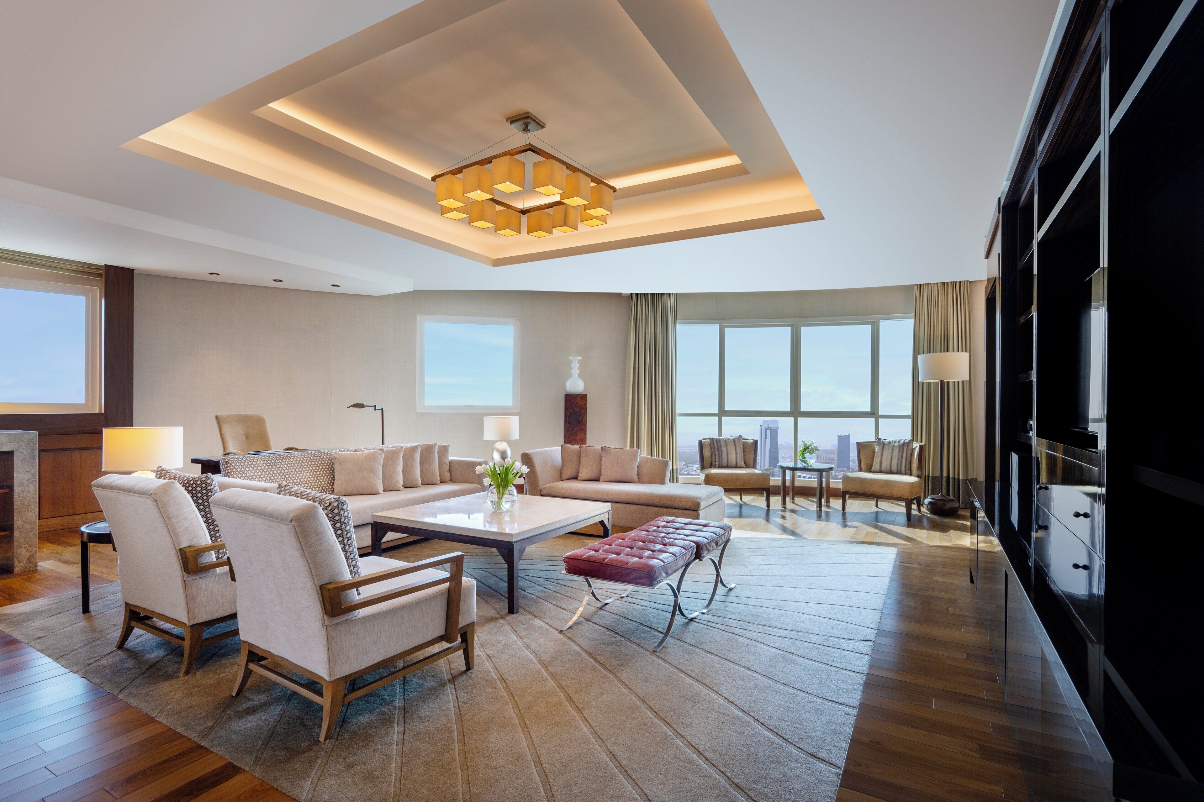 A spacious living room with a modern chandelier, large windows, and a view of the city skyline.