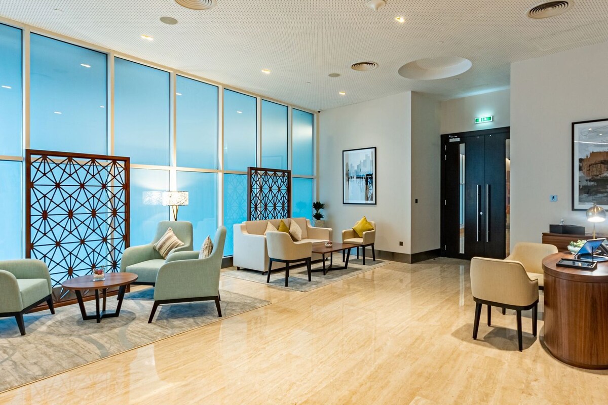 A modern lobby with seating areas, a reception desk, and a large window.