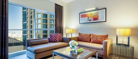 A modern living room with a sofa, a coffee table, and a view of a cityscape through large windows.