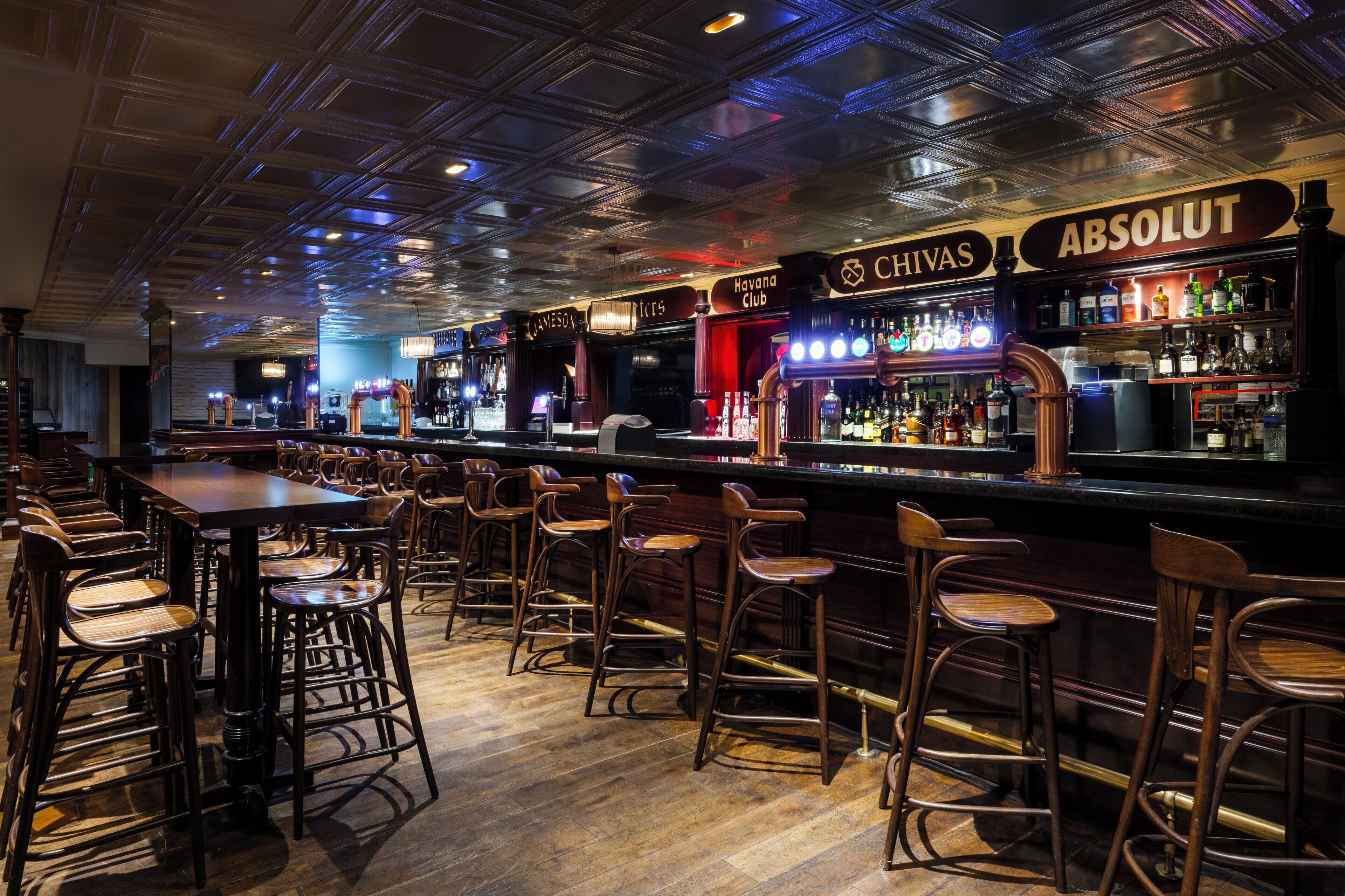 A bar area with stools and a long counter, featuring brands like Chivas and Absolut.