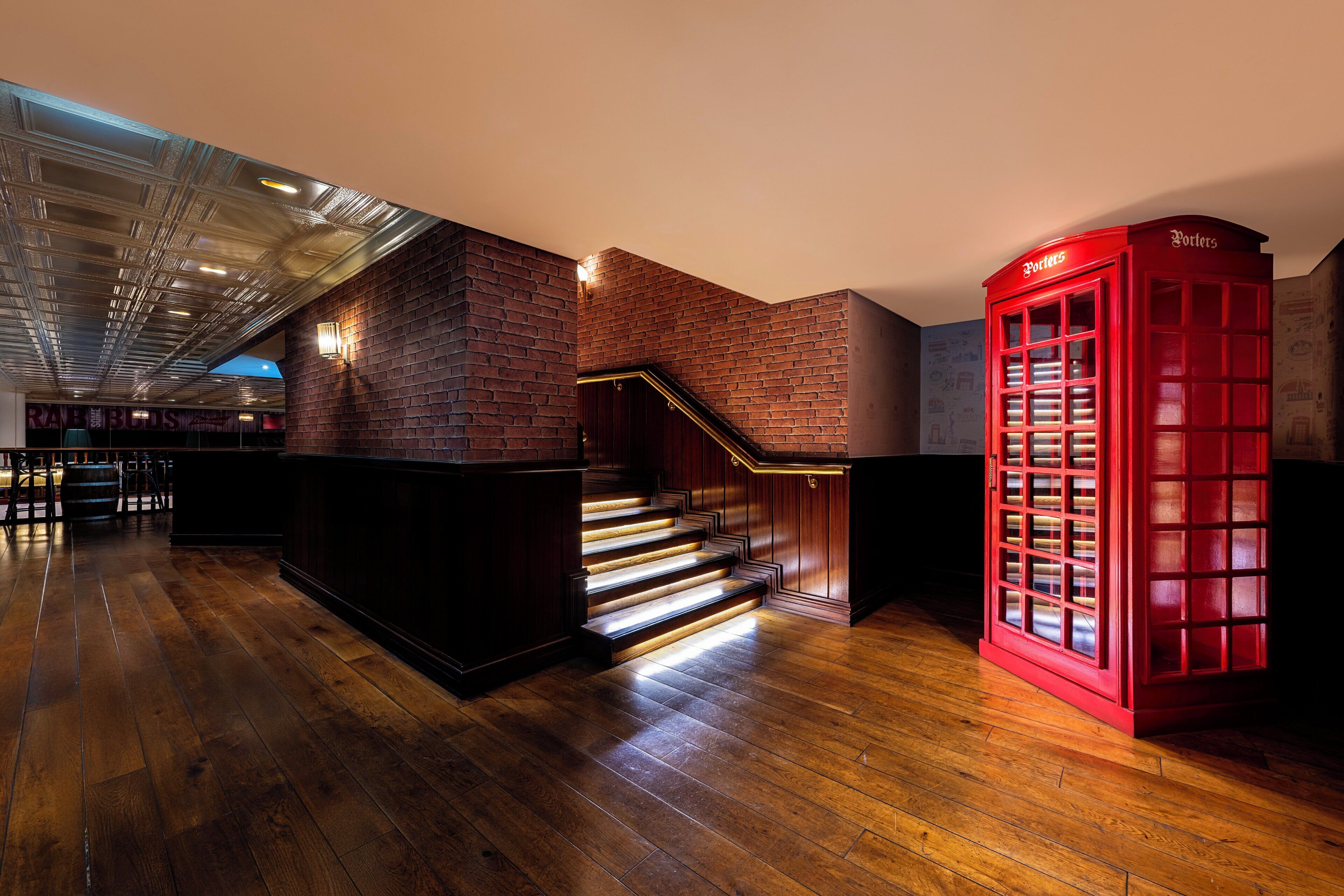 Un intérieur moderne avec un plancher en bois, un escalier et une cabine téléphonique rouge.