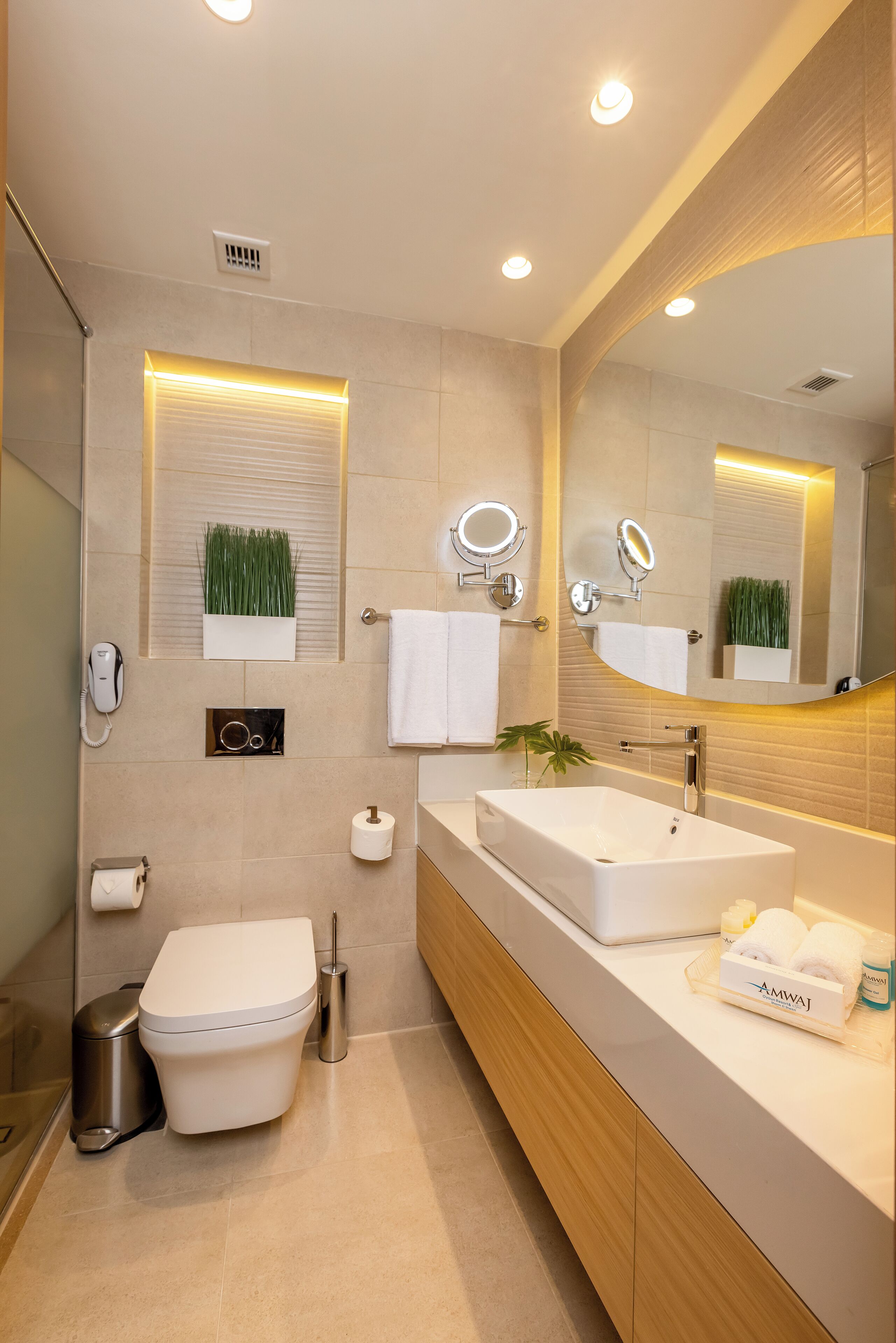 Un baño moderno con un espejo grande, un lavamanos blanco y un inodoro.