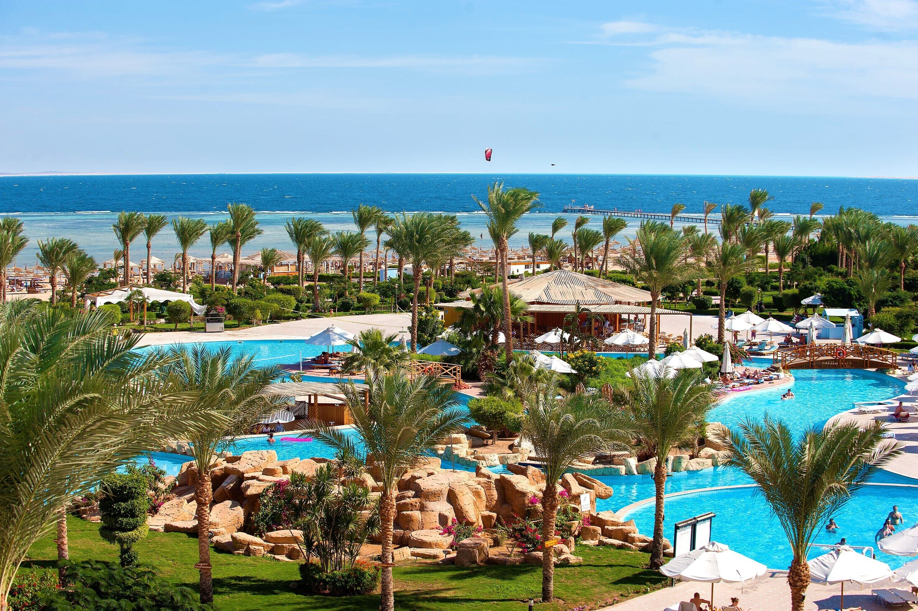 A resort with multiple swimming pools, palm trees, and a view of the sea.