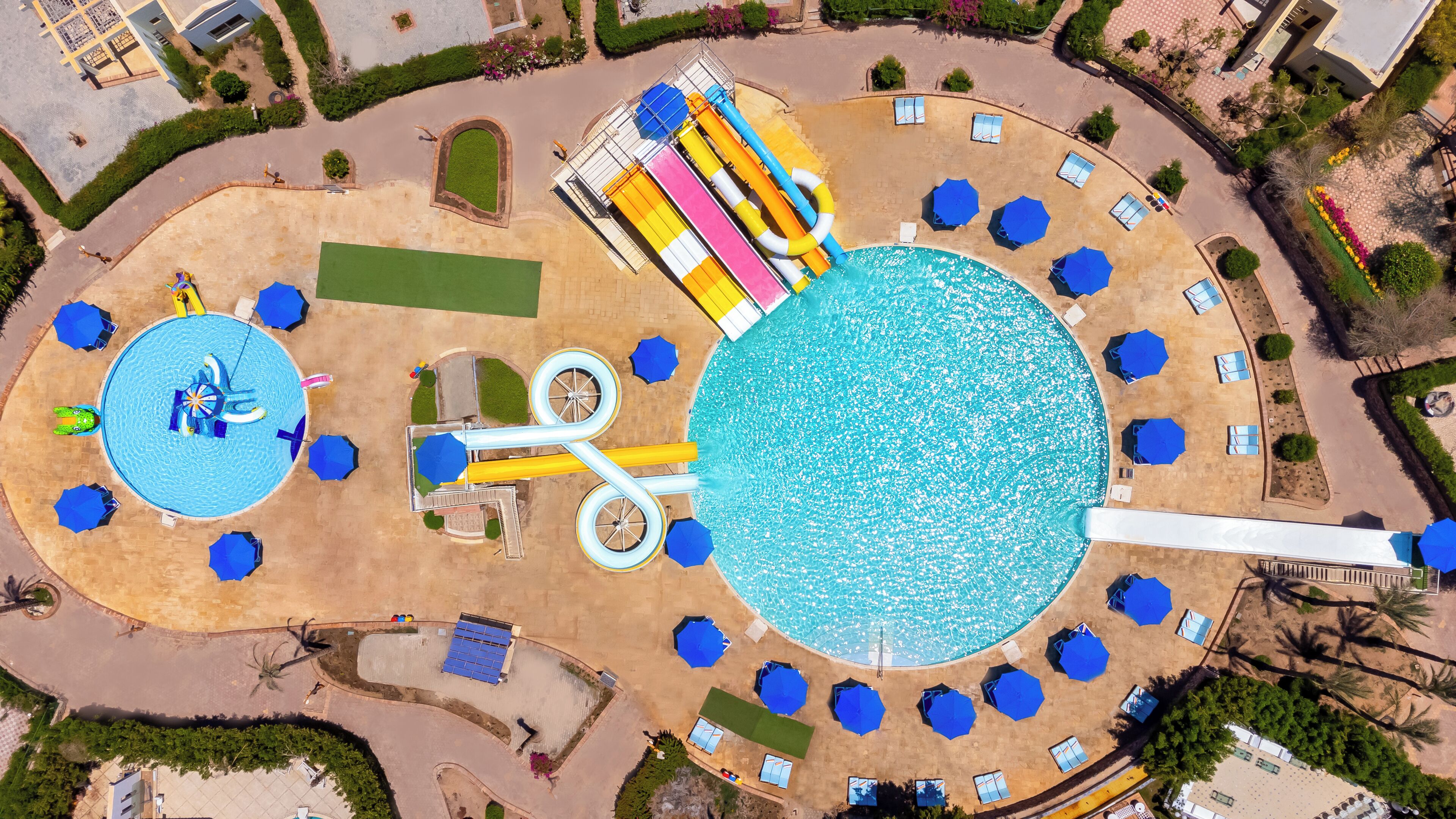 Vue aérienne d’un complexe hôtelier doté d’une grande piscine centrale, de plusieurs piscines plus petites et d’un toboggan aquatique.