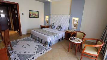 Una habitación de hotel con una cama grande, dos mesitas de noche, una pequeña mesa redonda con sillas, un tapete decorativo y un cuadro en la pared.