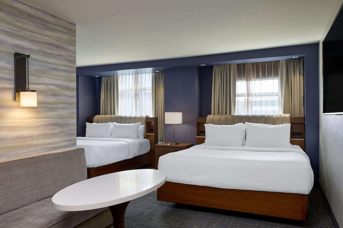 A hotel room with two beds, a sofa, a small table, and a lamp.