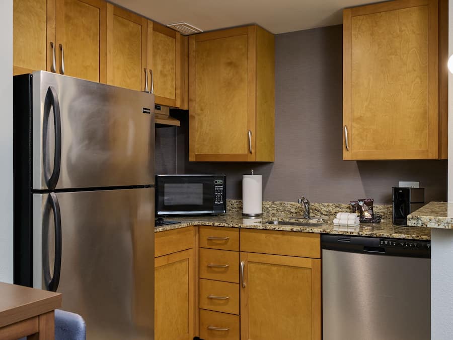 A modern kitchen with wooden cabinets, stainless steel appliances, a granite countertop, and a built-in dishwasher.