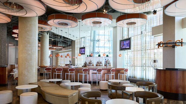 Een moderne bar met ronde tafels, zachte zitplaatsen en een houten toog.