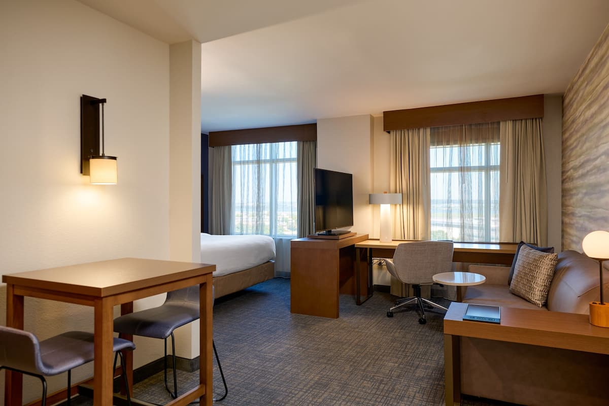 A hotel room with a bed, a desk, a chair, a sofa, a TV, and a lamp.