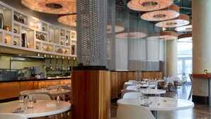 Een modern restaurantinterieur met ronde tafels, witte stoelen en een centrale decoratieve kolom.