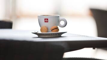 Una taza blanca con un logotipo, dos galletas sobre un platito y un fondo desenfocado.