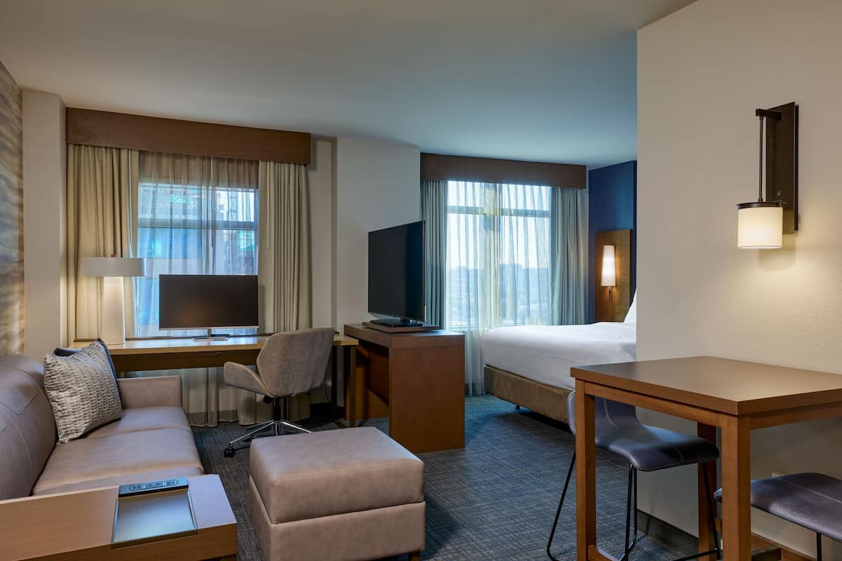 A hotel room with a sofa, desk, TV, and a bed.