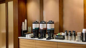 Una estación de café con varios dispensadores, vasos desechables y un molinillo.