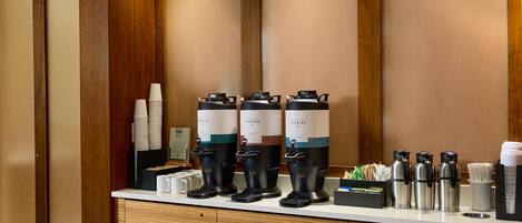 Una estación de café con varios dispensadores, vasos desechables y un molinillo.