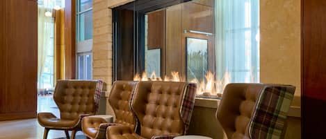 A lobby with leather armchairs, a fireplace, and large windows.
