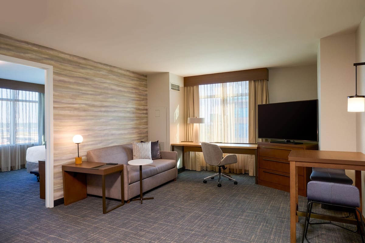 A hotel room with a sofa, a desk, a television, and a chair.