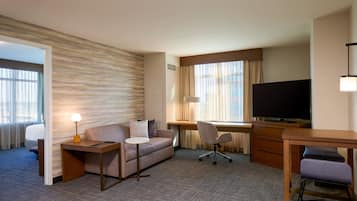 A hotel room with a sofa, a desk, a television, and a chair.