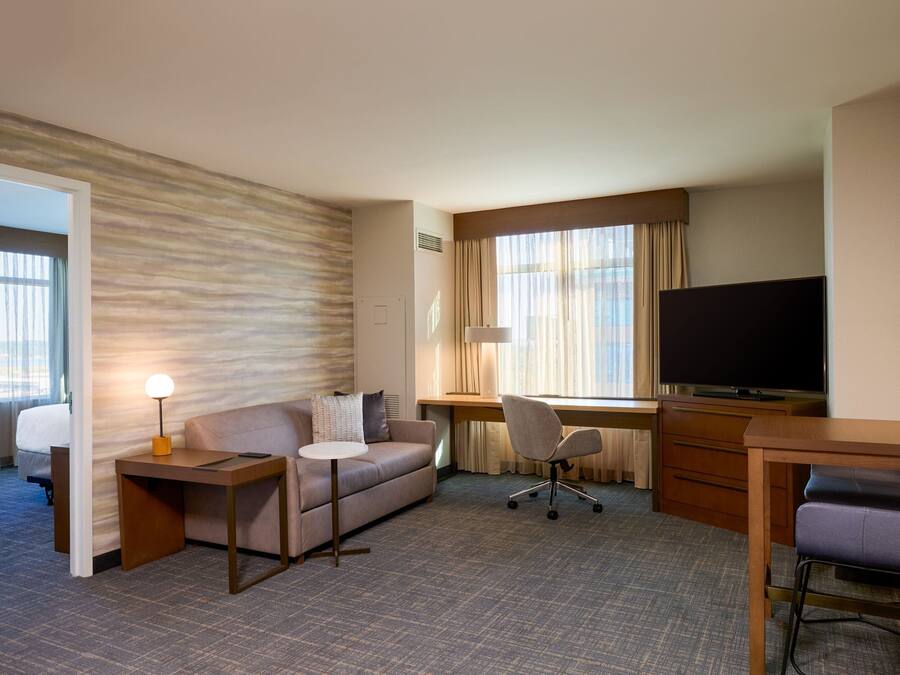 A hotel room with a sofa, a desk, a television, and a chair.
