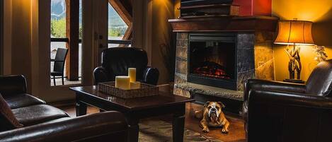 A cozy living room with a fireplace, leather furniture, and a dog.