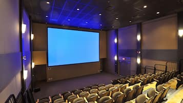 A movie theater with rows of seats, a large screen, and wall-mounted speakers.