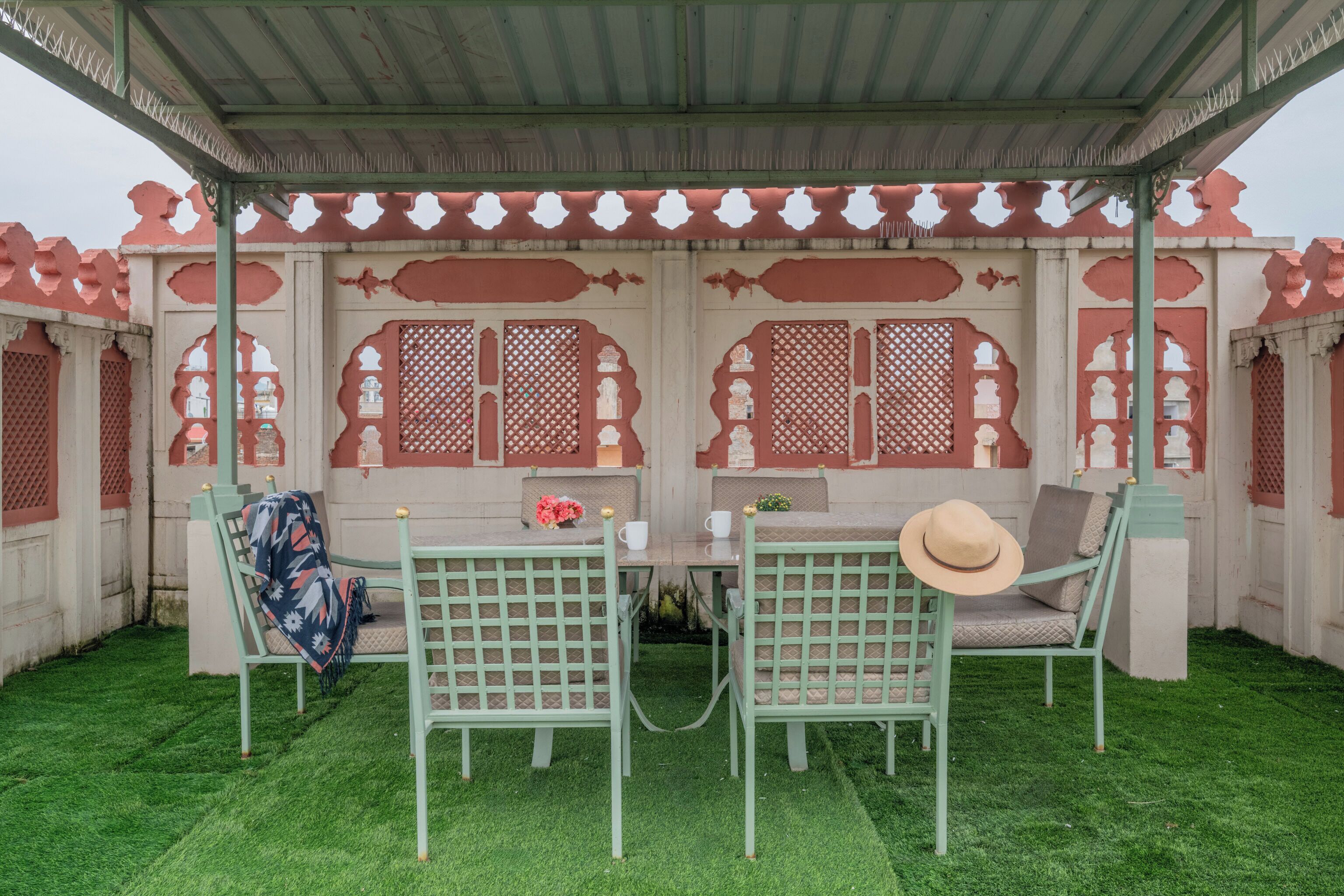 A covered outdoor seating area with two green chairs, a table, and a hat on one of the chairs.