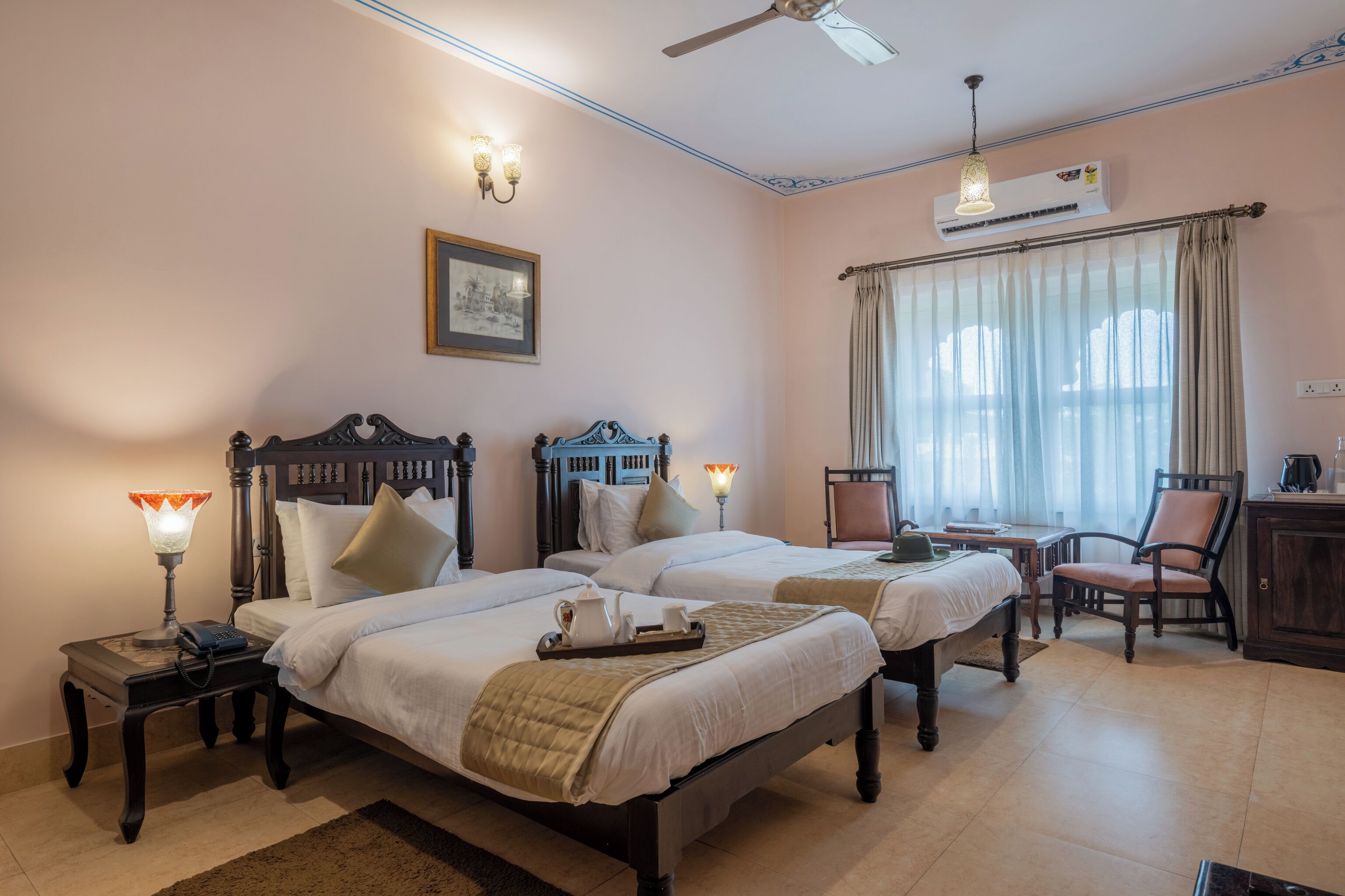 Quarto de hotel com duas camas, uma escrivaninha, uma cadeira, um abajur e um quadro na parede.