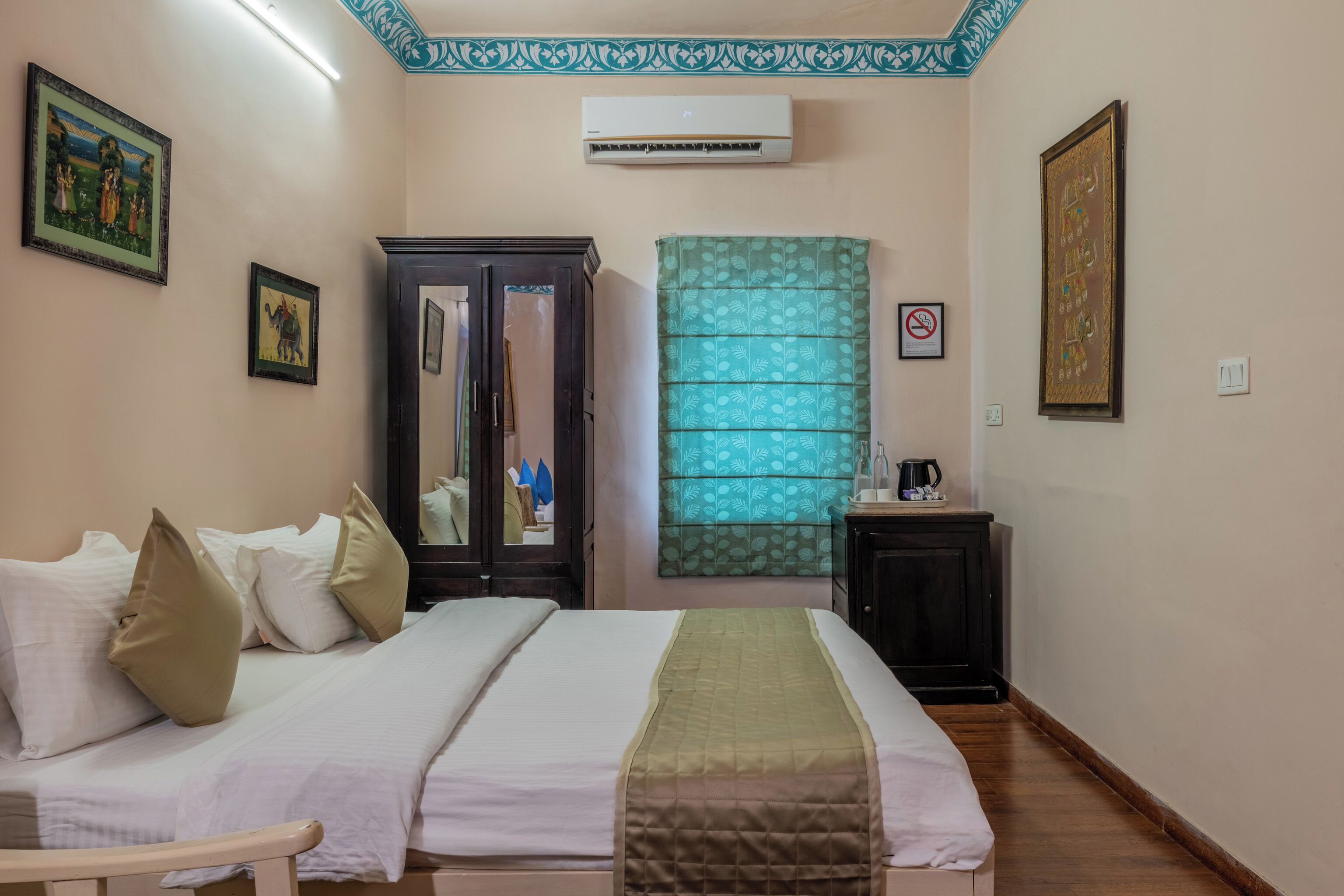 A hotel room with a bed, a wardrobe, a mirror, a green curtain, and a framed picture on the wall.