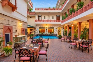 Un patio con piscina, zona de comedor con mesas y sillas, y un restaurante.