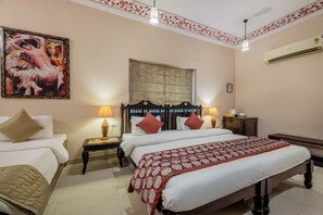 A hotel room with two beds, a large painting, a window, and an air conditioning unit. - Suryaa Villa - A City Centre Hotel (Jaipur)