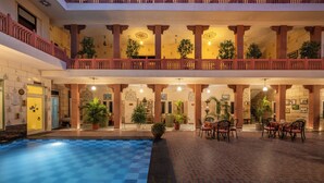 A hotel atrium with a pool, multiple levels, and potted plants. - Suryaa Villa - A City Centre Hotel (Jaipur)