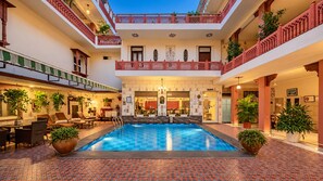 Un vestíbulo de hotel con piscina central, varios balcones y zonas de estar interiores.