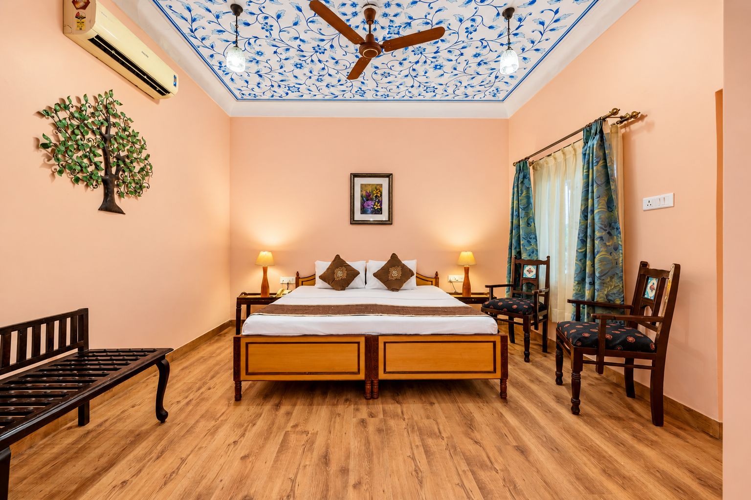 Un dormitorio con una cama de madera, dos mesitas de noche, un banco, un ventilador de techo y un aire acondicionado de pared.