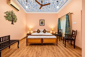 Un dormitorio con una cama de madera, dos mesitas de noche, un banco, un ventilador de techo y un aire acondicionado de pared.