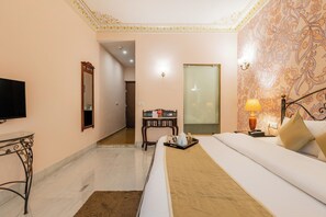 A hotel room with a bed, bedside table, lamp, and a television. - Suryaa Villa - A City Centre Hotel (Jaipur)