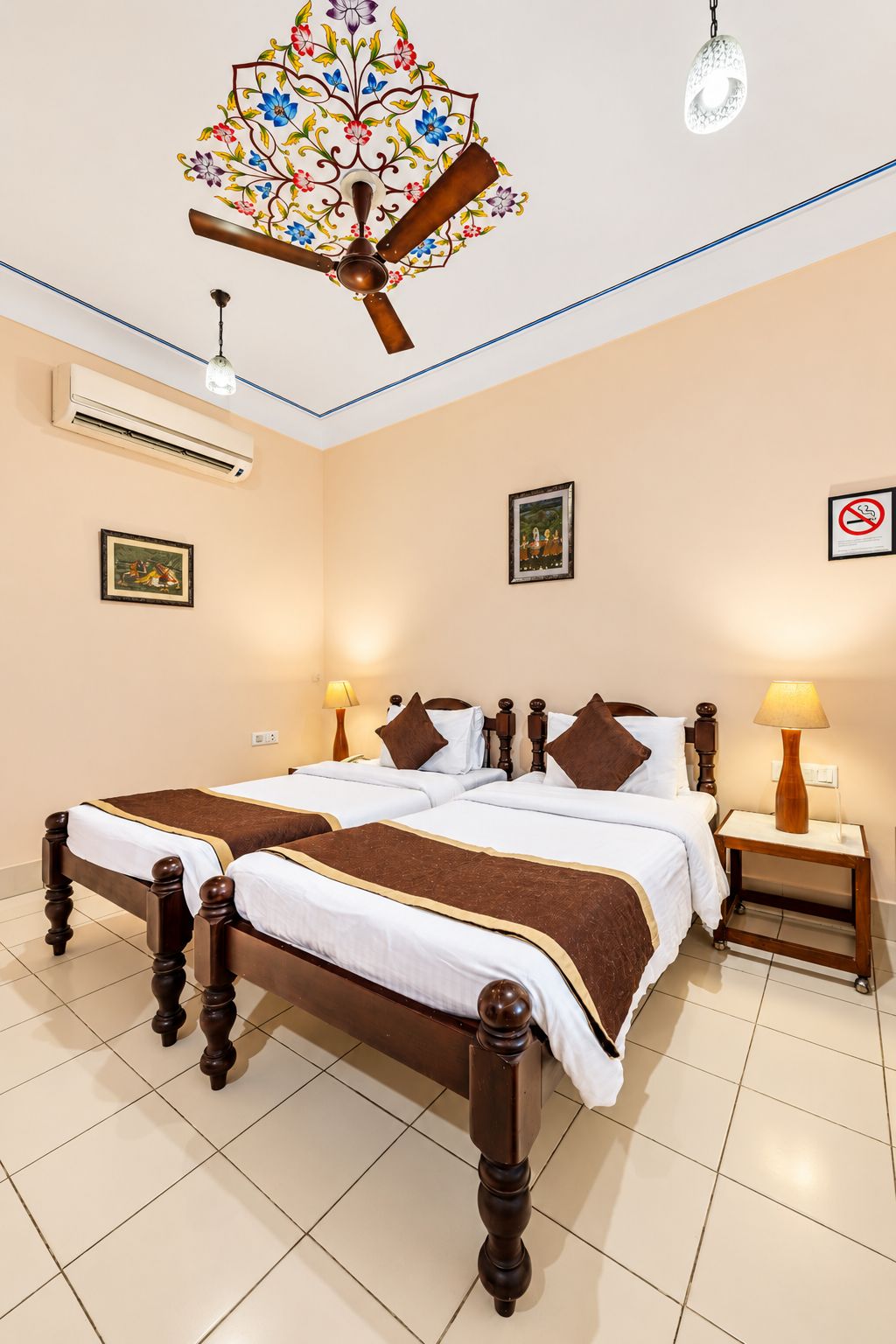 A hotel room with a double bed, two bedside tables, a ceiling fan, an air conditioning unit, and a wall-mounted artwork.