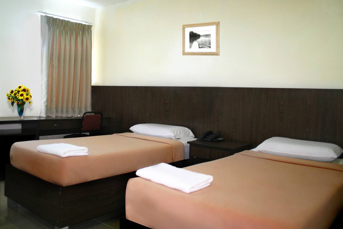 Ein Hotelzimmer mit zwei Betten, einem Schreibtisch mit Stuhl, einer Vase mit Blumen und einem gerahmten Bild an der Wand.