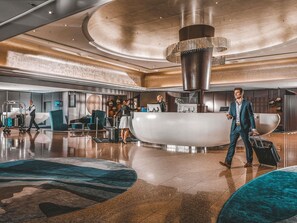 A modern lobby with a central reception desk, seating areas, and a large decorative column.