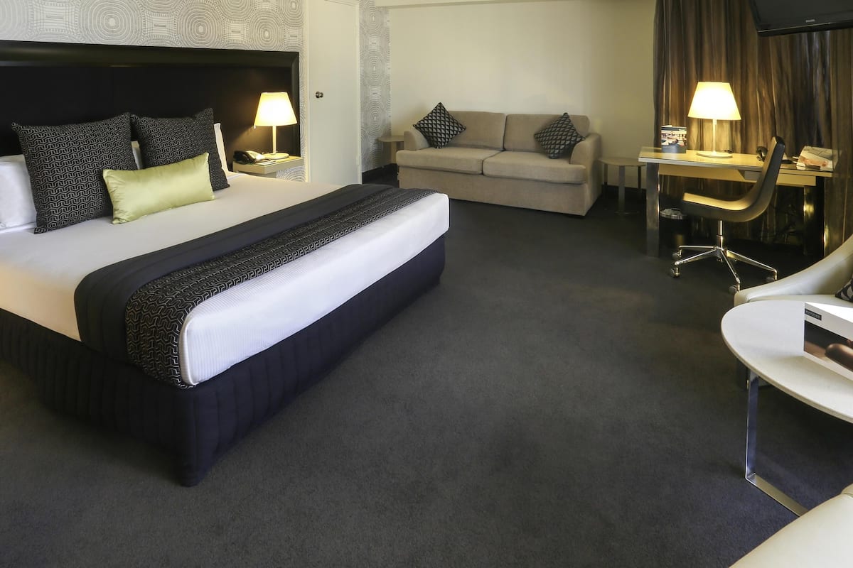 A hotel room with a large bed, a sofa, a desk with a chair, and a television.