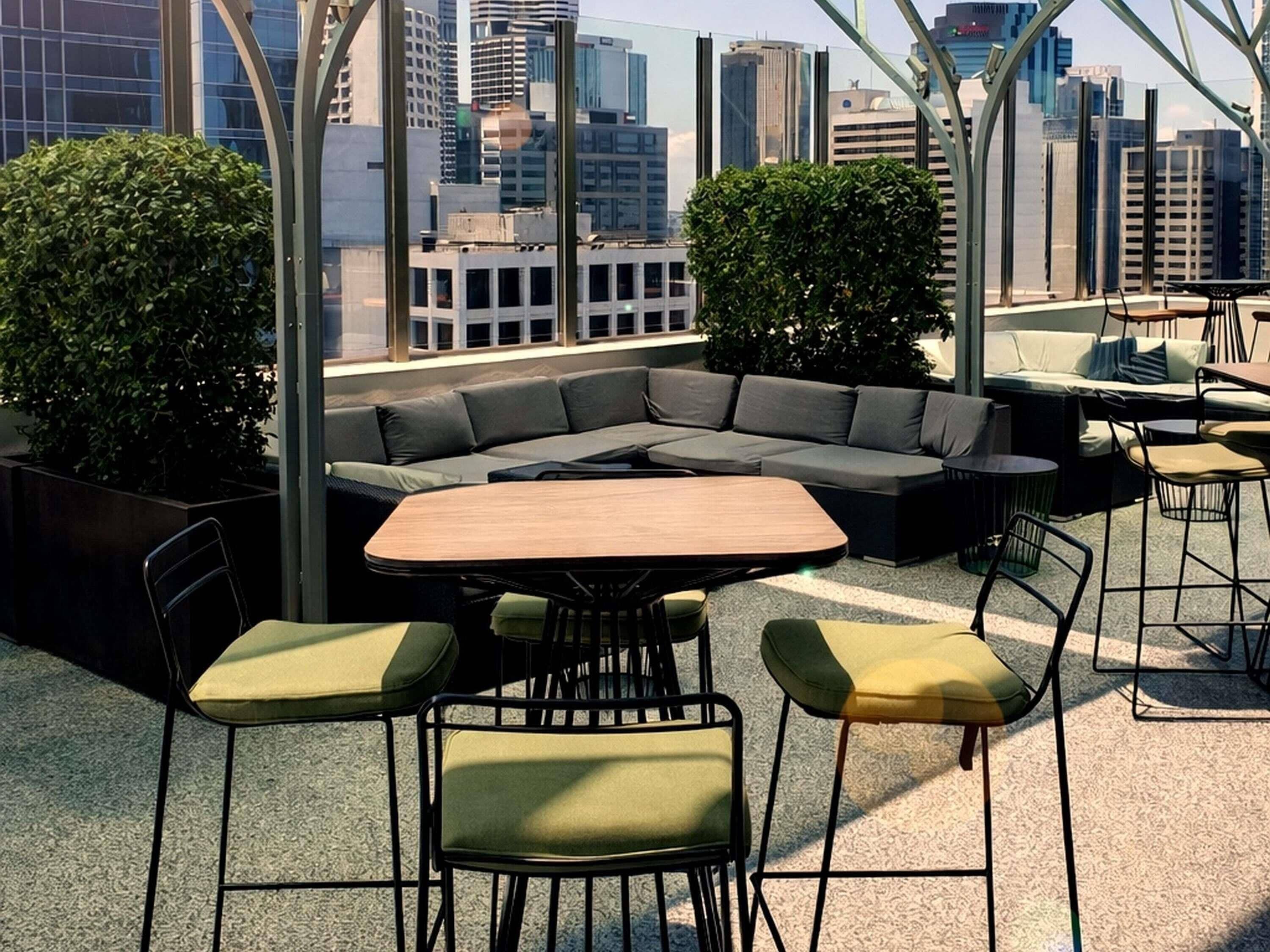 Un salón en la azotea con un sofá modular, una mesa redonda y taburetes de bar.